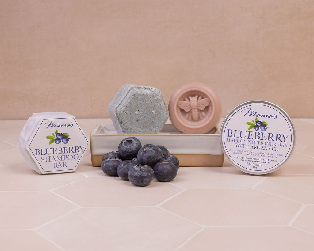 Blueberry hair conditioner bar and solid blueberry shampoo bar on a soap dish and with blueberries