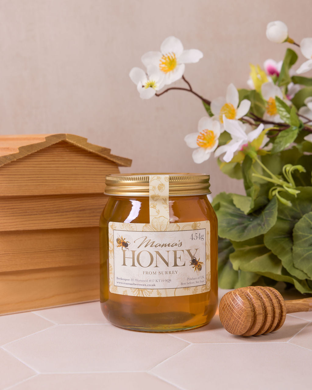 Jar of honey with a wooden honey dipper and a beehive on a beige surface.