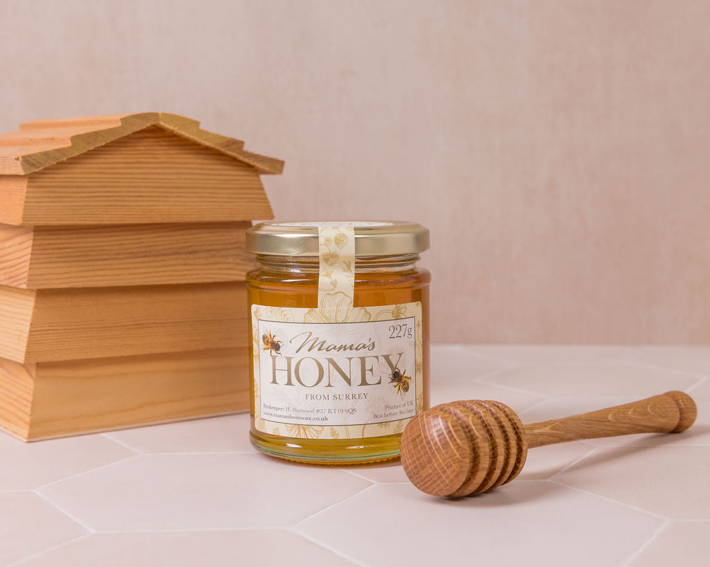 Jar of honey with a wooden honey dipper and beehive-shaped container on a light background