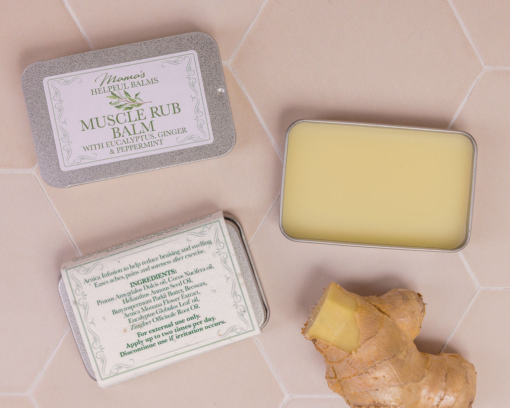 Helpful Muscle Balm in a tin with a piece of ginger on a tiles surface
