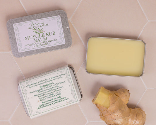 Helpful Muscle Balm in a tin with a piece of ginger on a tiles surface