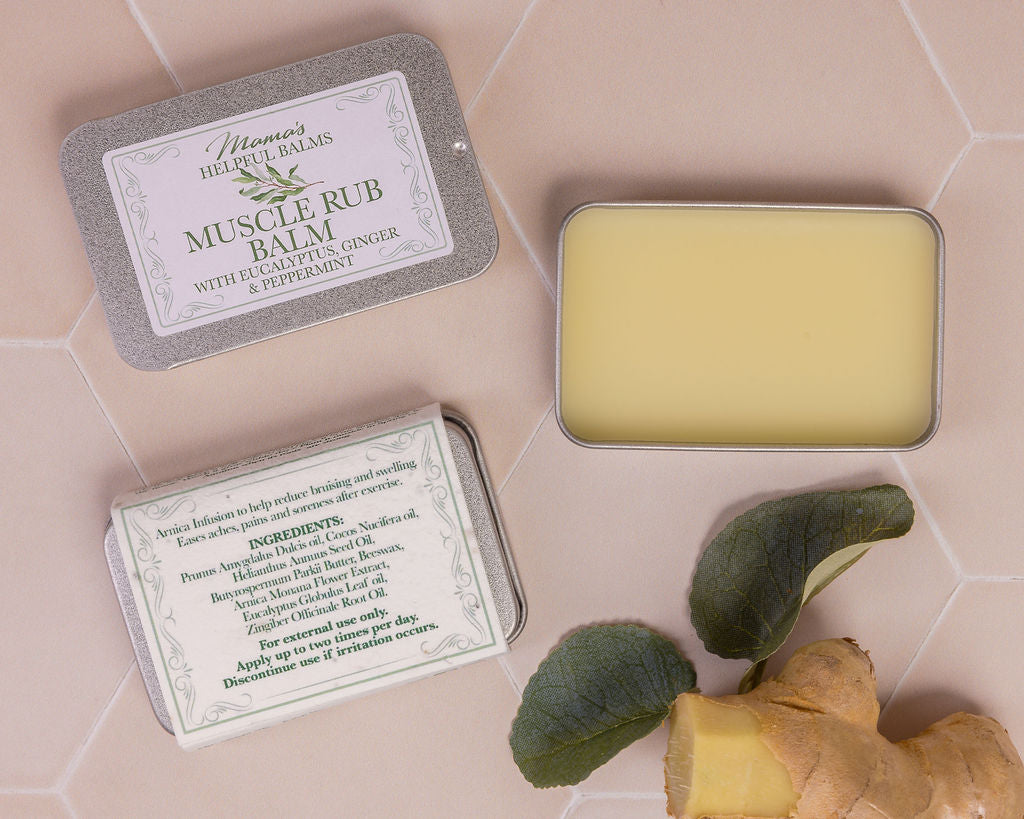 Muscle rub balm in a tin with ginger root and peppermint leaves  on a tiled surface