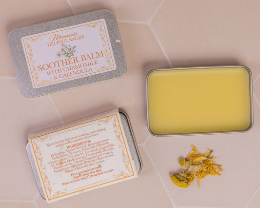 Open tin of Mama's soother balm with calendula and chamomile petals on a tiled surface