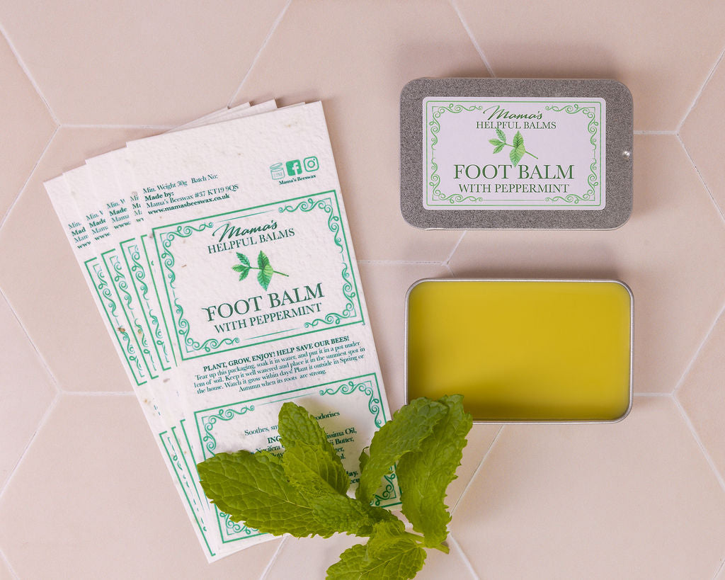 Mama's Helpful Foot balm with seeded paper labels and mint leaves on a tiled surface